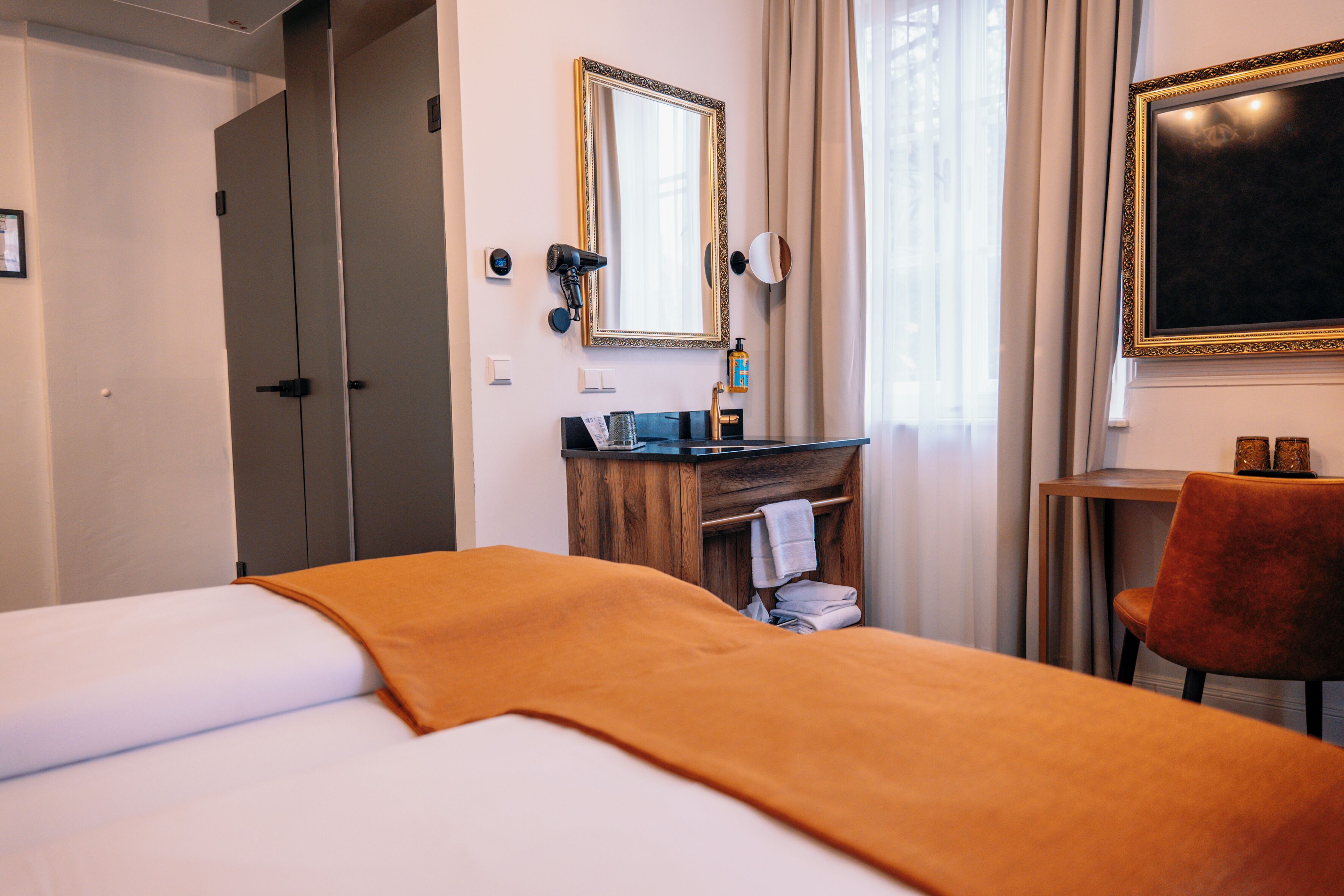 A hotel room with a bed, a wooden dresser, a mirror, and a desk with a chair.