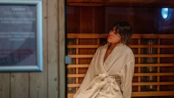 A person in a white bathrobe sitting in a wooden sauna room with a framed sign on the wall.