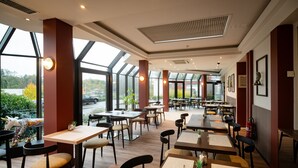 Een ruim restaurant met hoge plafonds, grote ramen en diverse zitmogelijkheden.