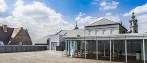 Un patio amplio con un edificio de techo de vidrio, una construcción tradicional con techo inclinado y una estatua al fondo.