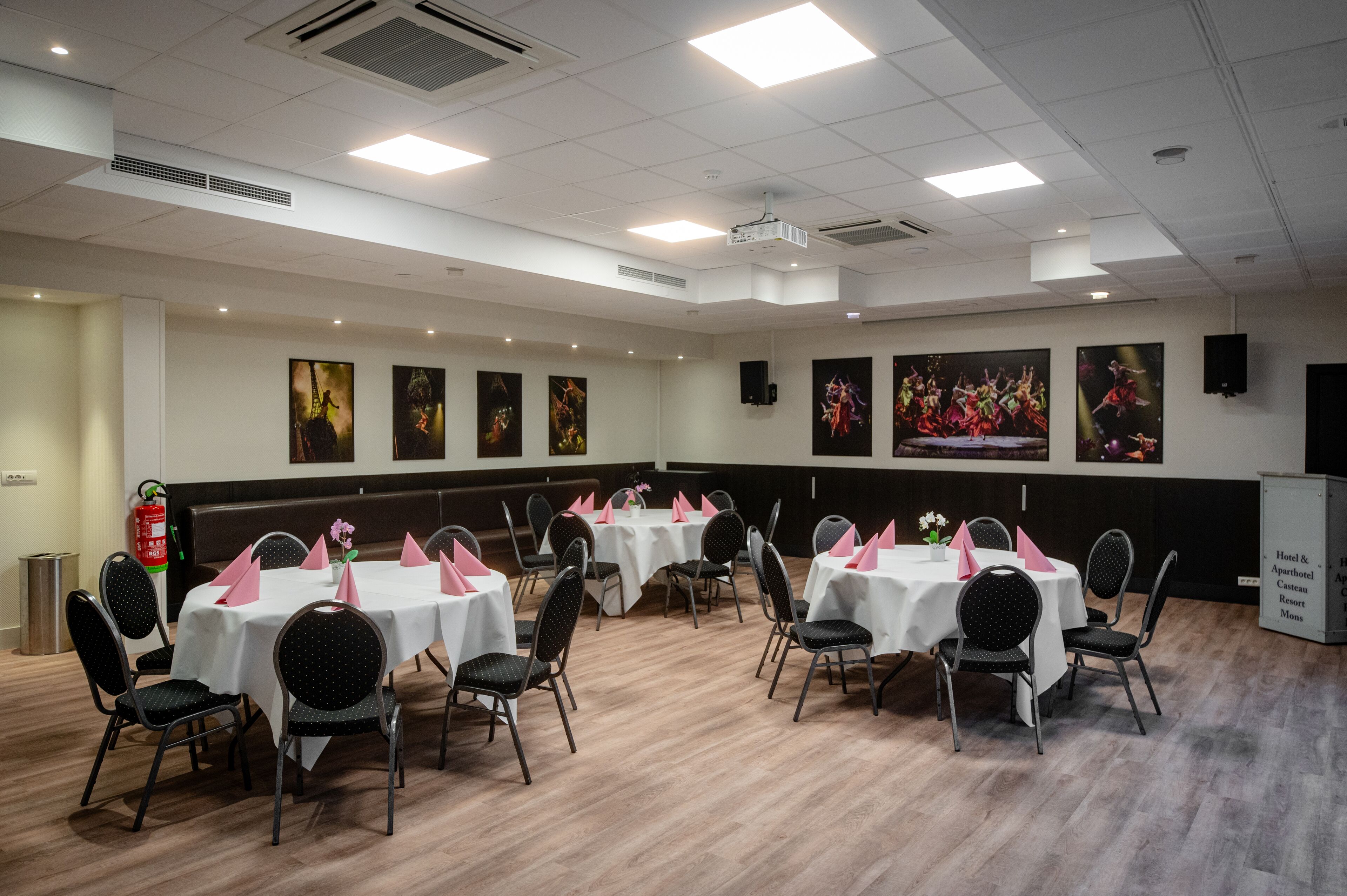 Un salón de conferencias con varias mesas y sillas, manteles blancos y servilletas rosas.