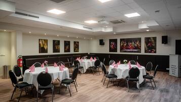 Un salón de conferencias con varias mesas y sillas, manteles blancos y servilletas rosas.