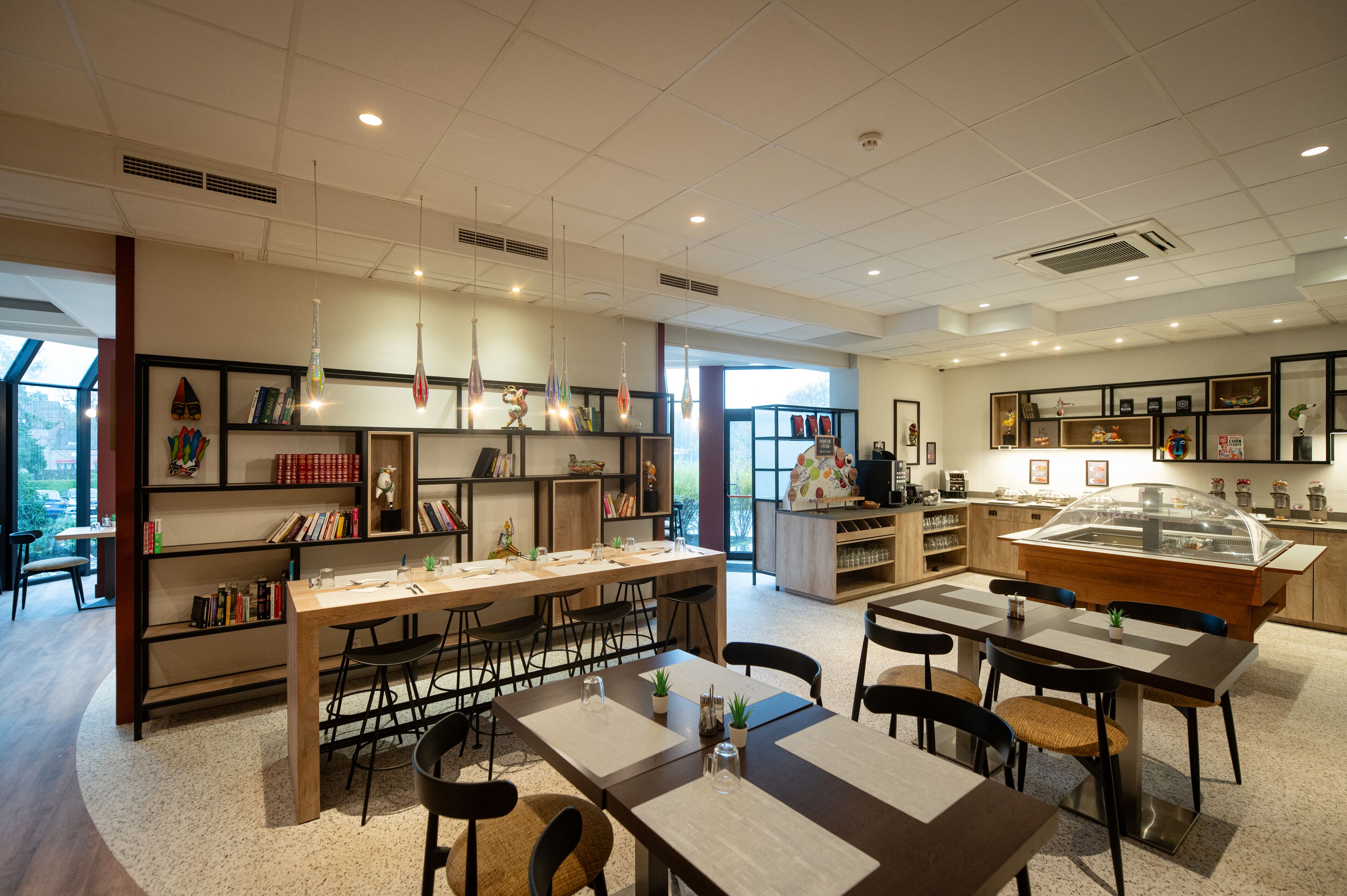 A modern cafe with a long communal table, individual tables, and a variety of seating options.