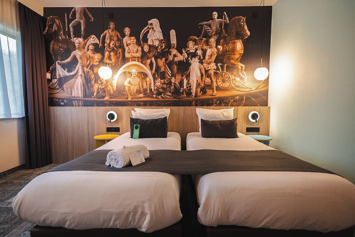 A hotel room with two beds, a large wall mural, and bedside lamps.