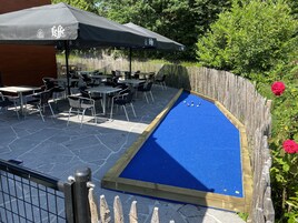 Un espace extérieur aménagé avec des tables et des chaises, un terrain de croquet bleu et une clôture en bois.