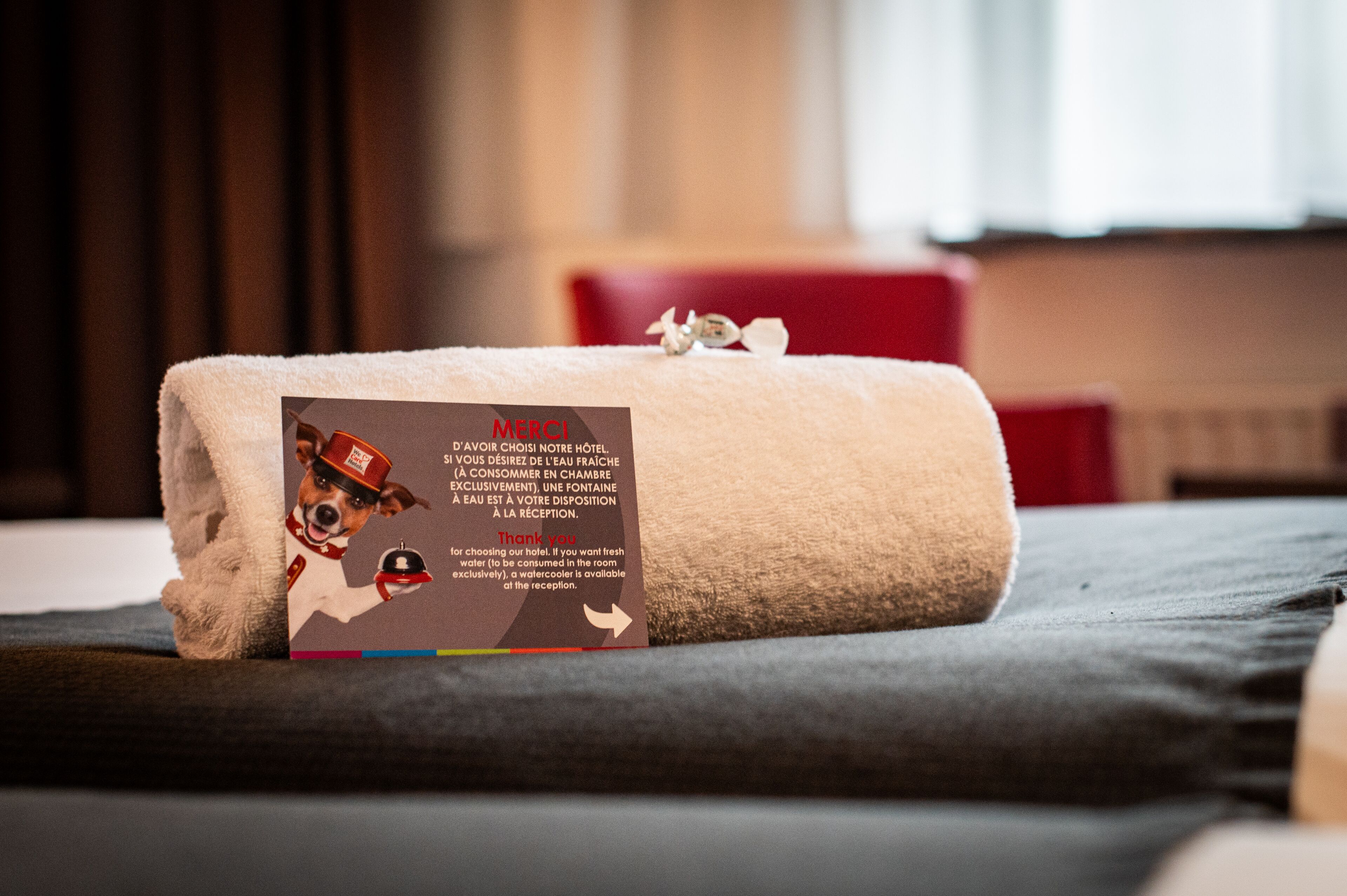 A neatly folded white towel with a hotel service sign and a thank you note on a bed.
