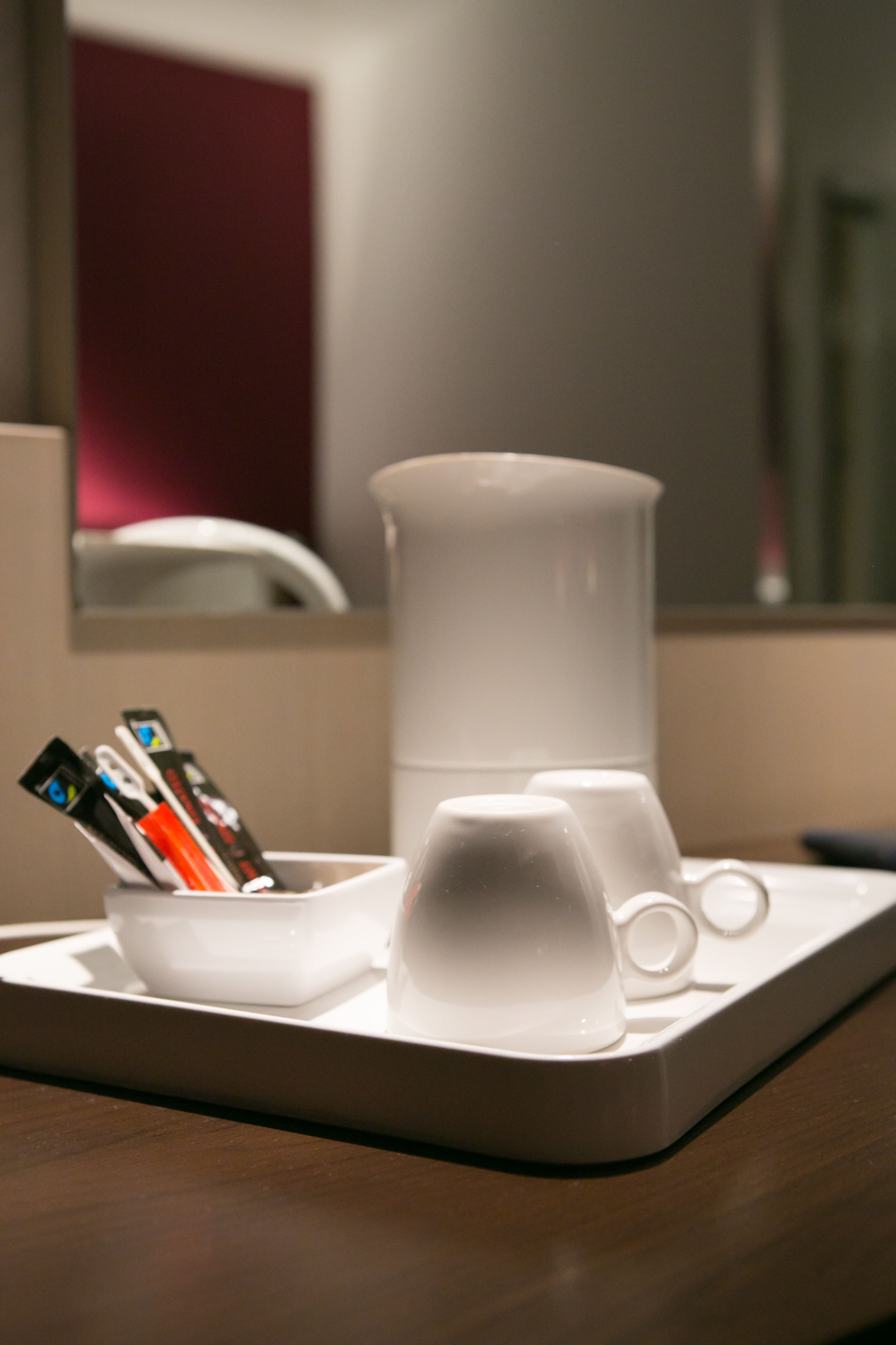 Una cafetera blanca y una taza sobre una bandeja en una habitación de hotel.
