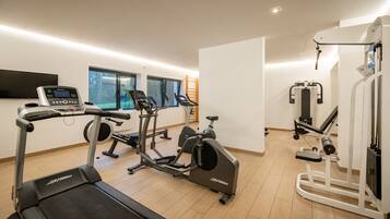 A modern gym with cardio machines, a weight bench, and a TV screen.