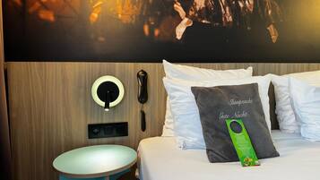 A hotel room with a bed, a bedside table, a wall-mounted phone, and a wall art piece.