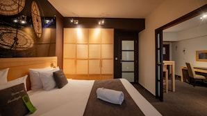 Une chambre d’hôtel avec un grand lit, une armoire en bois, un bureau avec une chaise et un miroir.