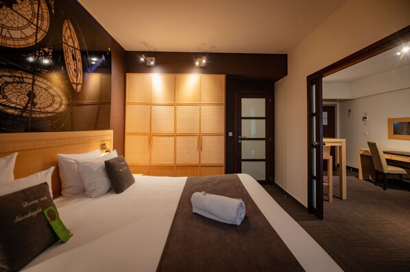A hotel room with a large bed, a wooden wardrobe, a desk with a chair, and a mirror. - Hotel & Aparthotel Casteau Resort Mons (Soignies)