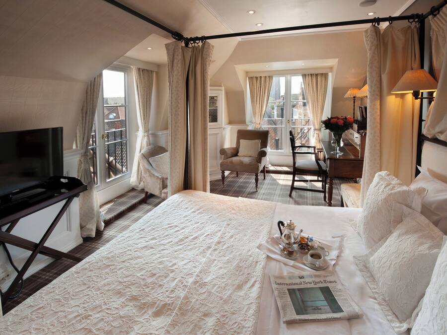 Een hotelkamer met een groot bed, een televisie, een zithoek met een tafel en stoelen, en een uitzicht op de stad door de ramen.