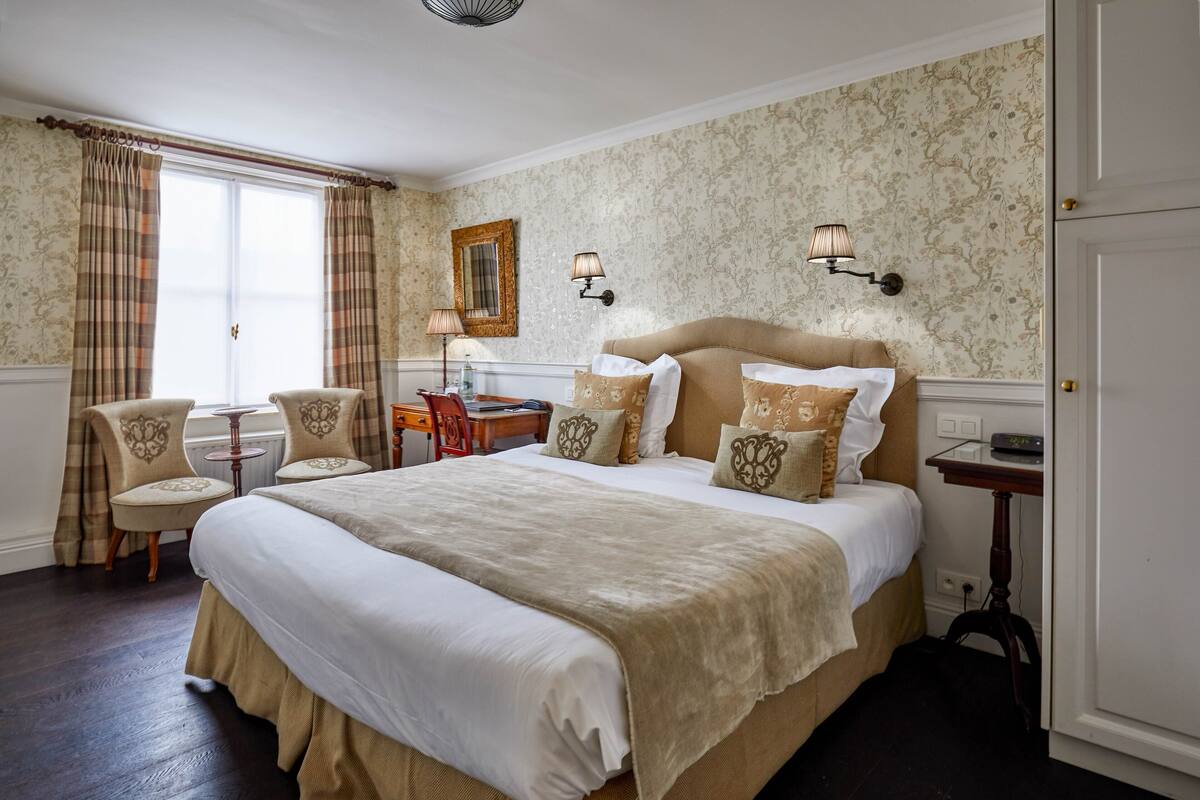 A hotel room with a large bed, two chairs, a desk, and a lamp.