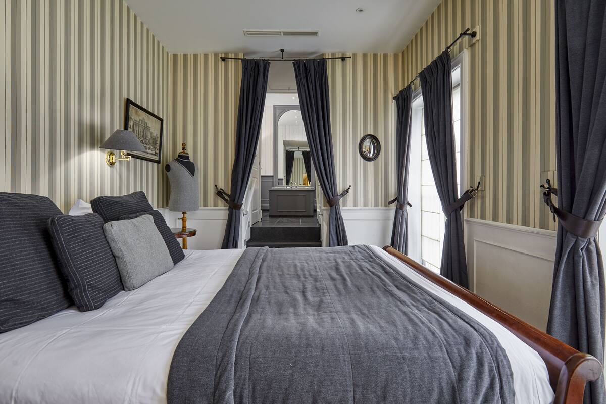 A hotel room with a large bed, striped wallpaper, and a view of the bathroom.