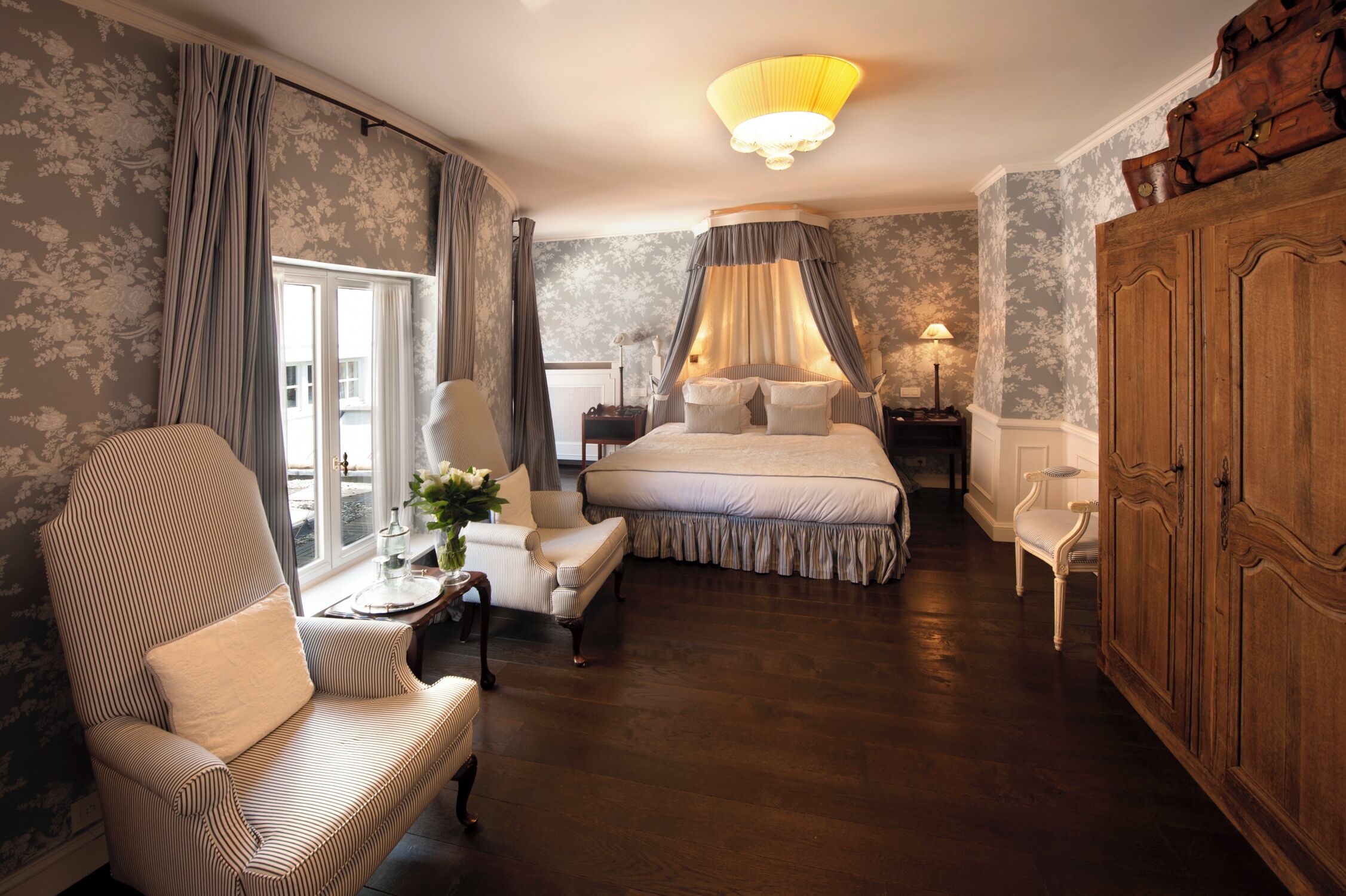 Une chambre à coucher avec un grand lit, un coin salon avec un fauteuil, une table de chevet et une armoire.