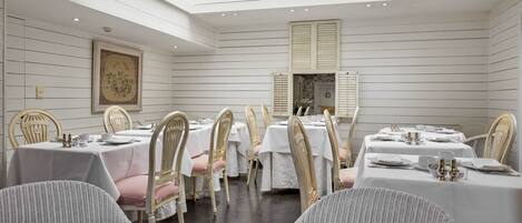 A dining area with white tables and chairs, a skylight, and a framed artwork on the wall.
