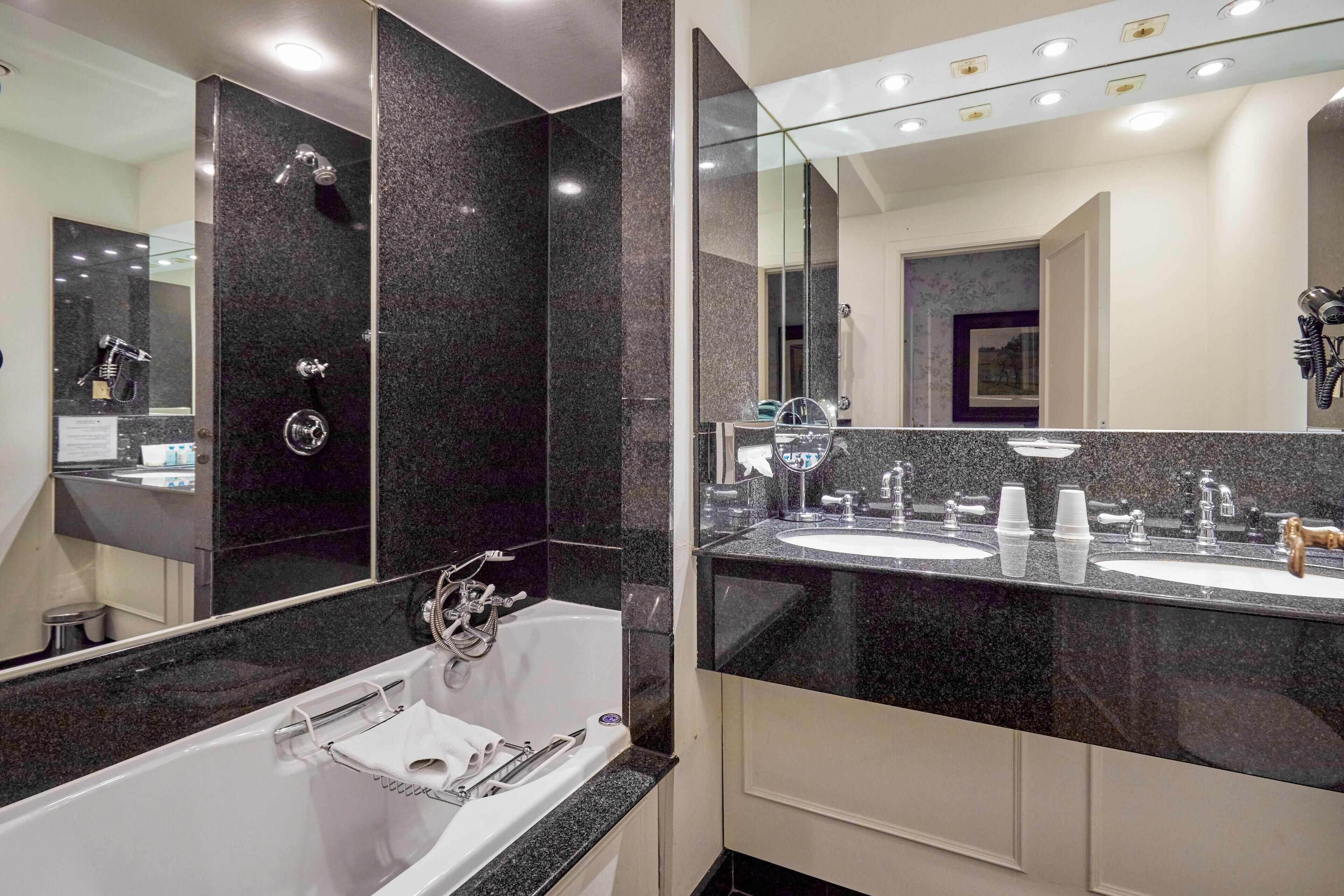 A modern bathroom with a large mirror, two sinks, a bathtub, and a vanity with a mirror.