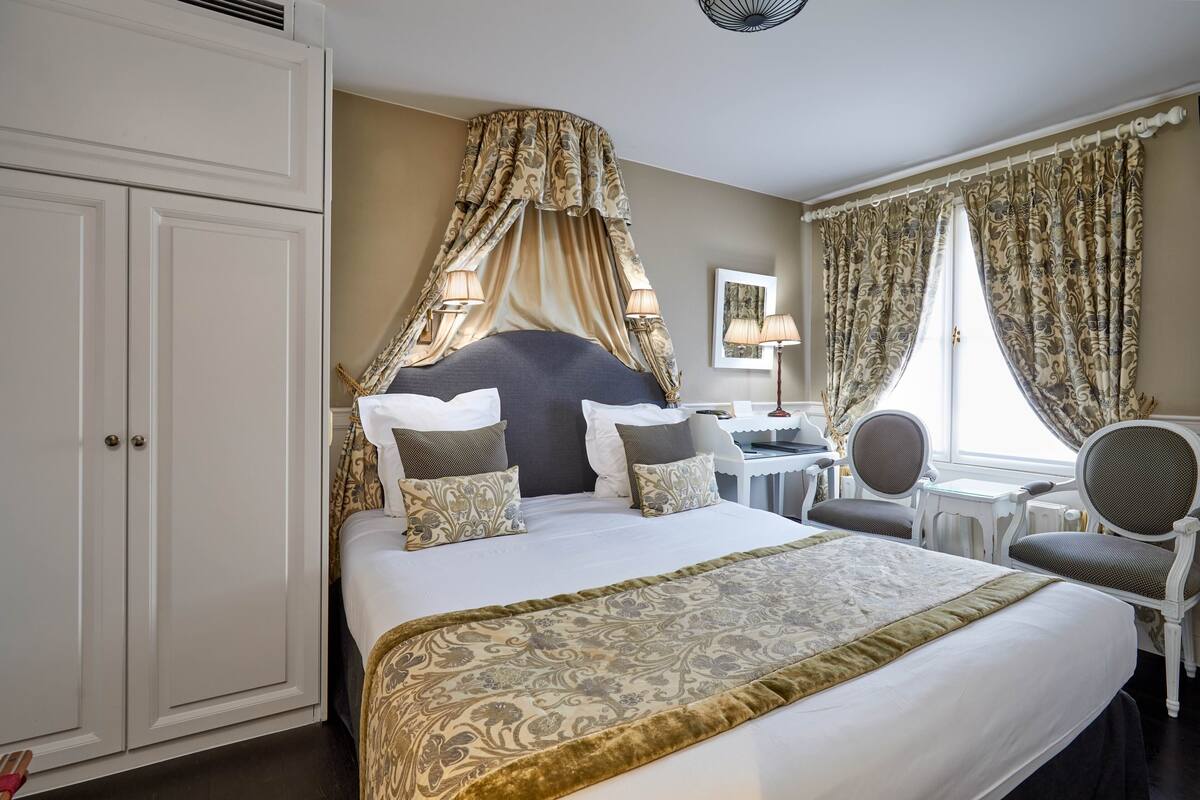 A hotel room with a large bed, a canopy bed, a desk with a chair, and a window with curtains.
