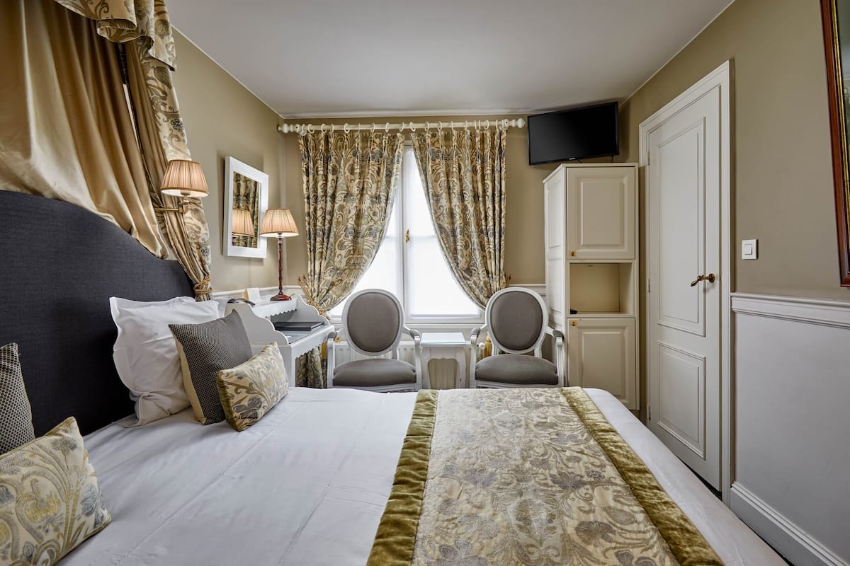 Une chambre d’hôtel comprenant un lit, deux chaises, un bureau, une télévision et une armoire.