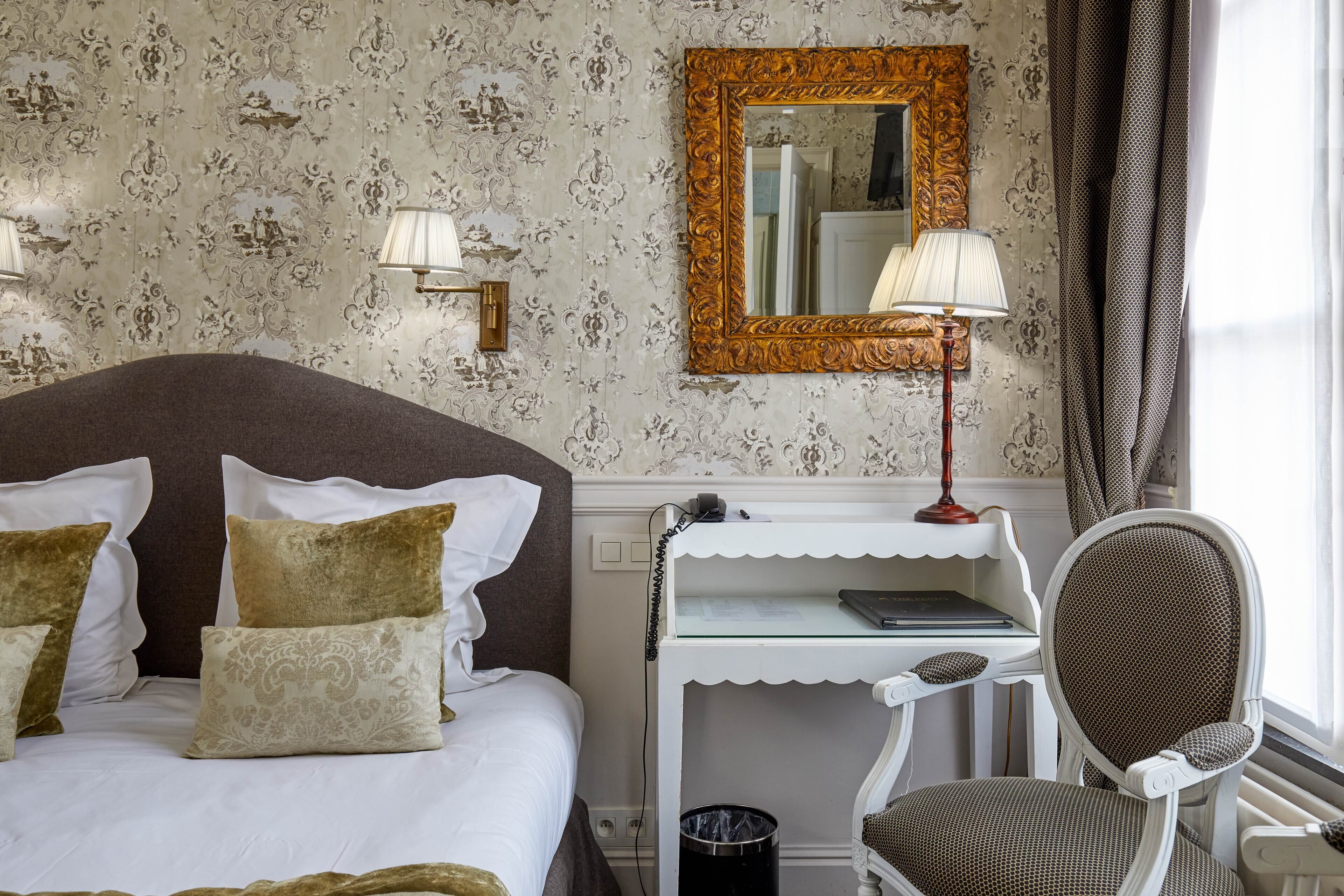 Een hotelkamer met een groot bed, een bureau met lamp, een stoel en een spiegel aan de muur.