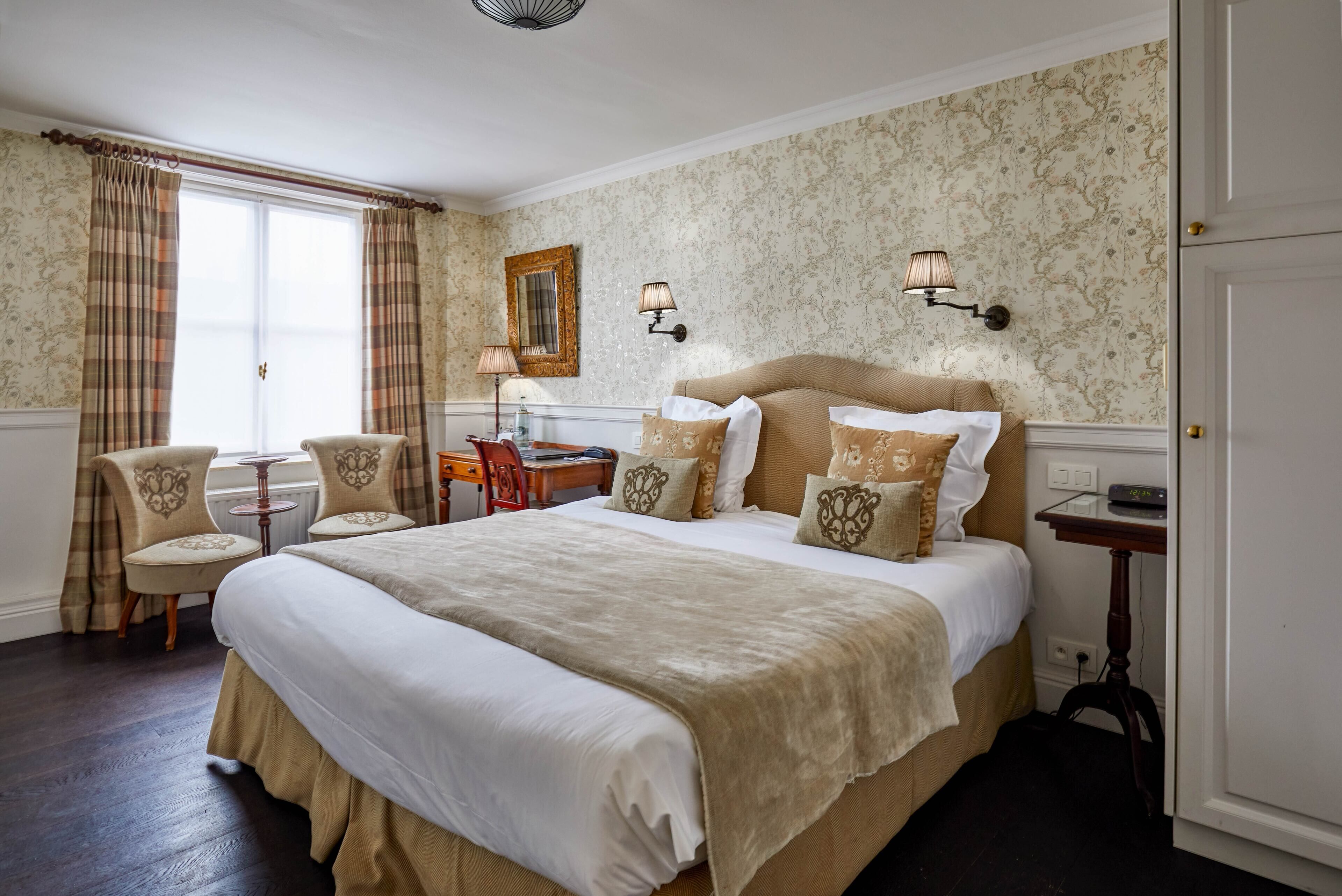 Une chambre d’hôtel avec un grand lit, deux fauteuils, un bureau et une lampe.