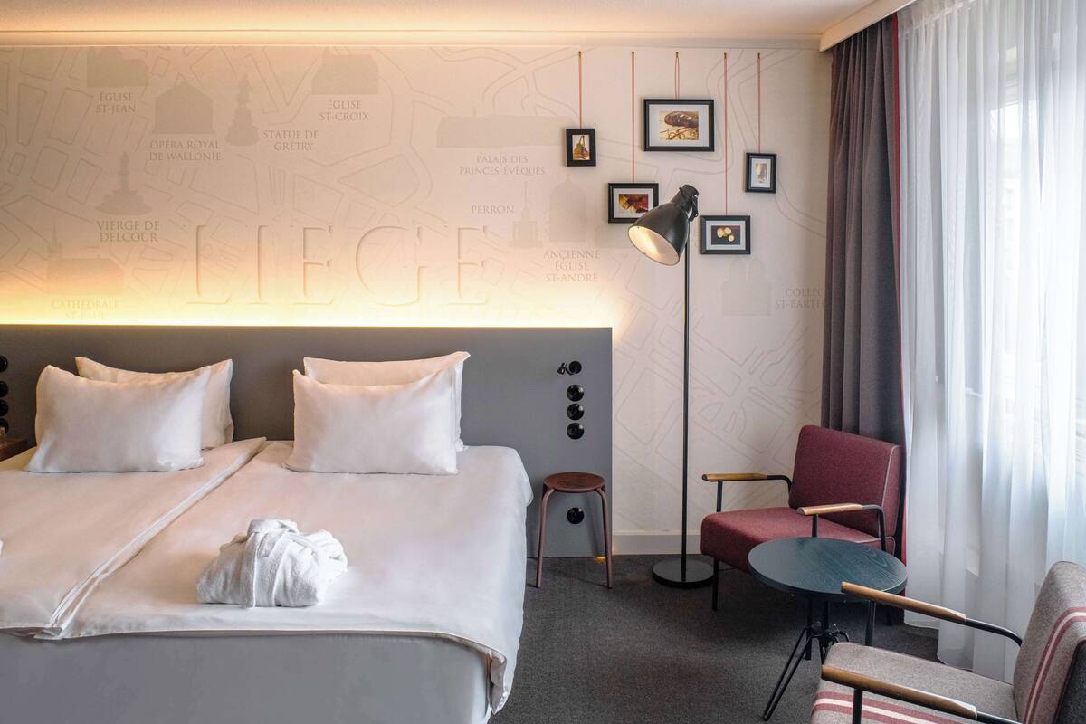 Quarto de hotel com uma cama grande, uma escrivaninha, uma cadeira e um mapa na parede.
