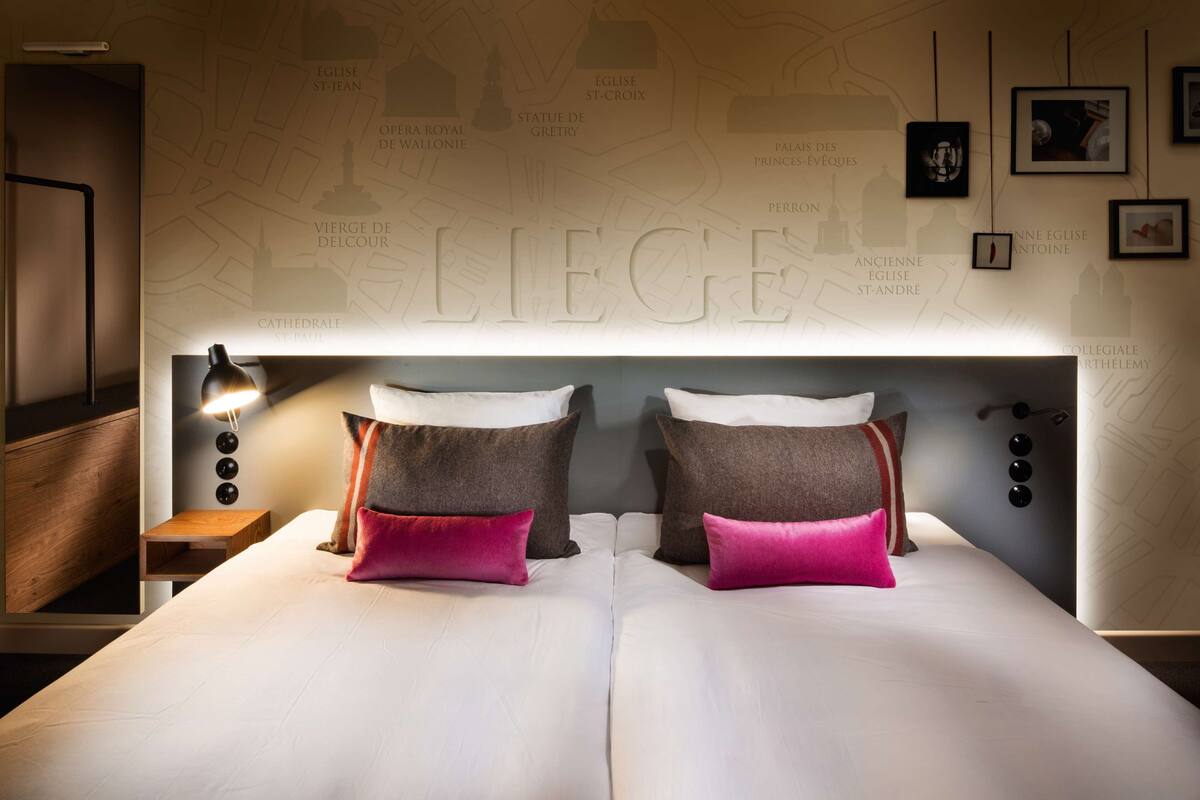 Quarto de hotel com cama, almofadas, mesa de cabeceira, abajur e parede com mapa.