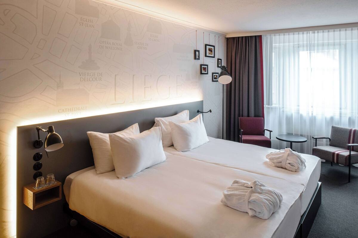 Quarto de hotel com duas camas, cabeceira com um mapa, uma mesa pequena e uma cadeira.