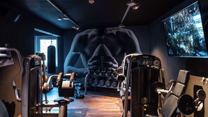 A gym with various exercise machines, a wall-mounted TV, and a window with natural light. - pentahotel Liège (Liege)