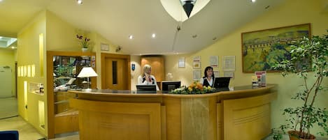 A reception area with a curved wooden desk, a receptionist, a computer, and a potted plant.