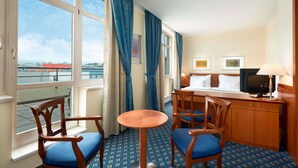Een hotelkamer met balkon, een bed met televisie, een bureau met lamp en twee stoelen.