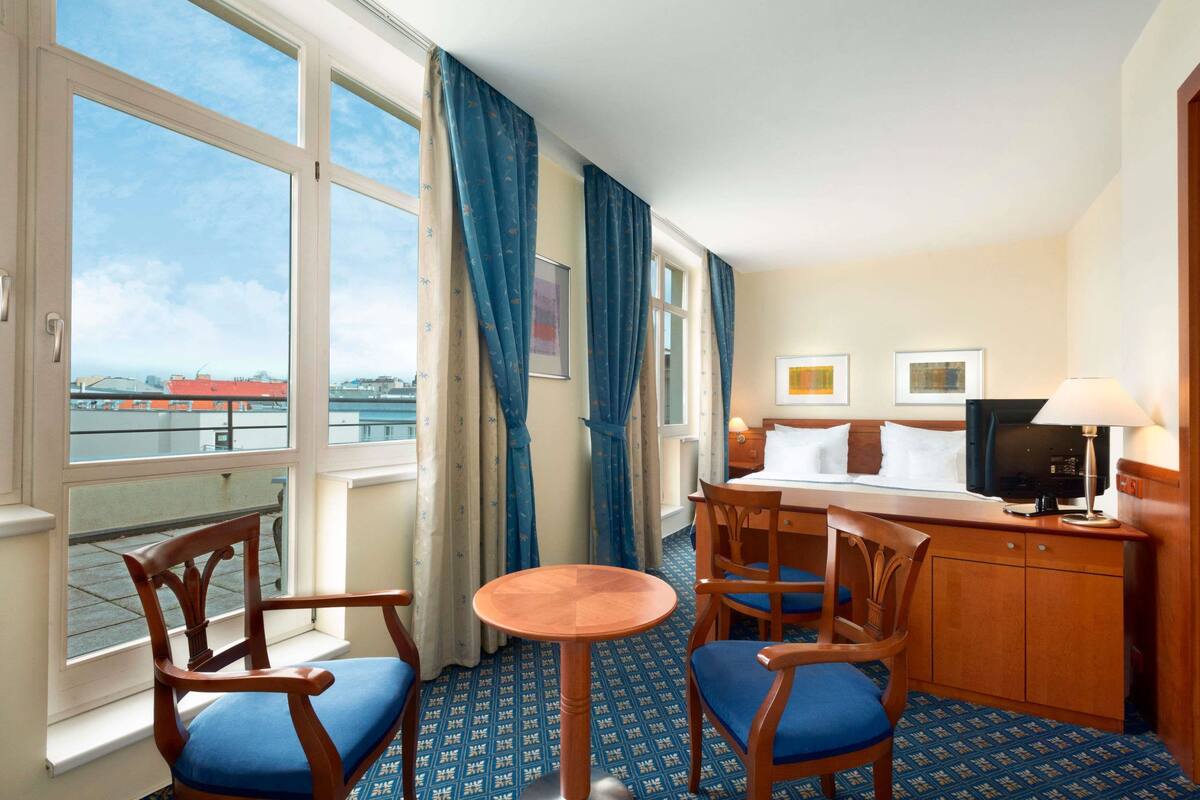 Une chambre d’hôtel avec un balcon, un lit avec une télévision, un bureau avec une lampe et deux chaises.