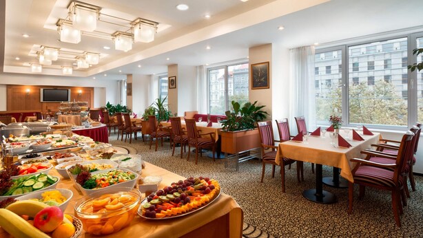 Een ruime eetruimte met meerdere tafels, een buffet met diverse gerechten en grote ramen met uitzicht op de stad.