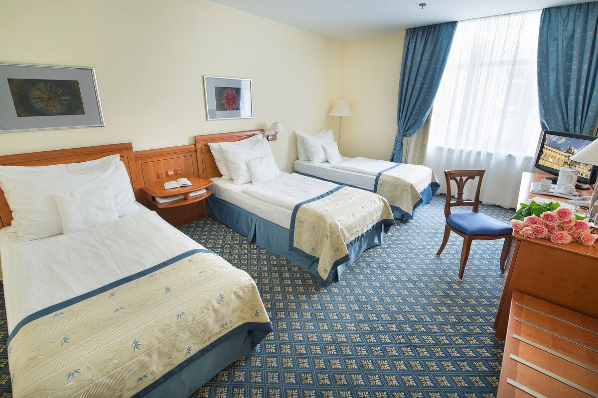 Une chambre d’hôtel avec deux lits, un bureau, une chaise, une lampe et un téléviseur.