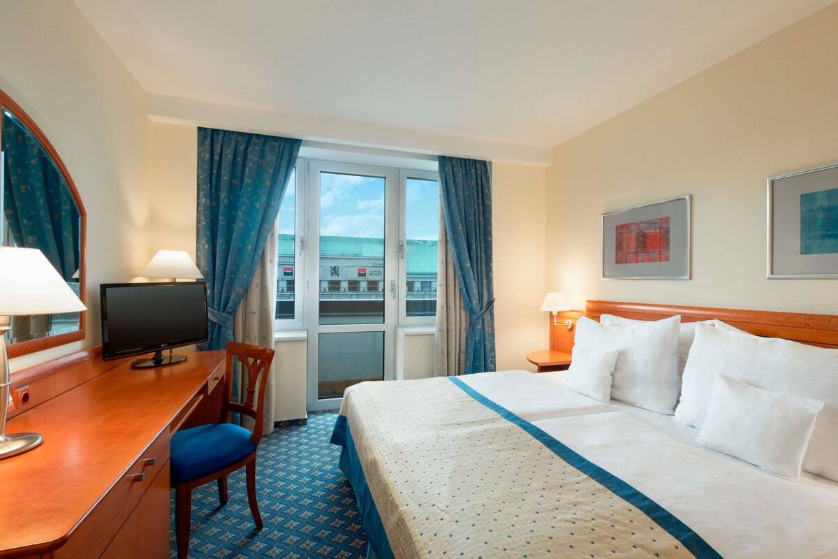 Une chambre d’hôtel avec un lit, un bureau avec un ordinateur, une chaise, une fenêtre avec des rideaux et une vue sur l’extérieur.