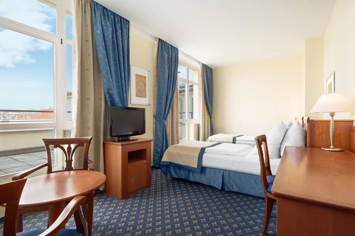 Une chambre d’hôtel avec un lit, un téléviseur posé sur un meuble en bois, un bureau avec une lampe et une chaise.