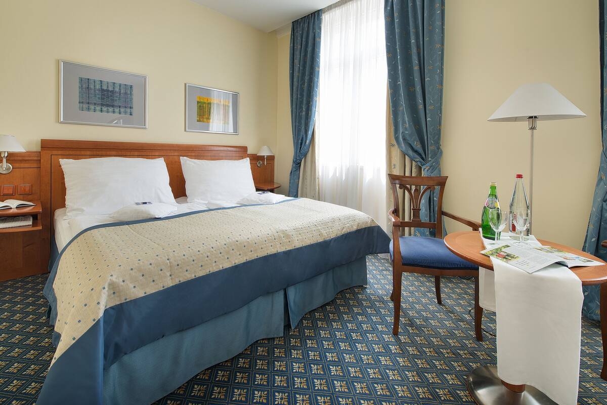 Une chambre d’hôtel avec un lit, une chaise, une table avec une lampe et deux tableaux encadrés au mur.