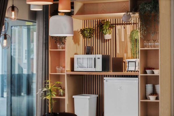 Una cocina moderna con estantes de madera, microondas, refrigerador y plantas colgantes.