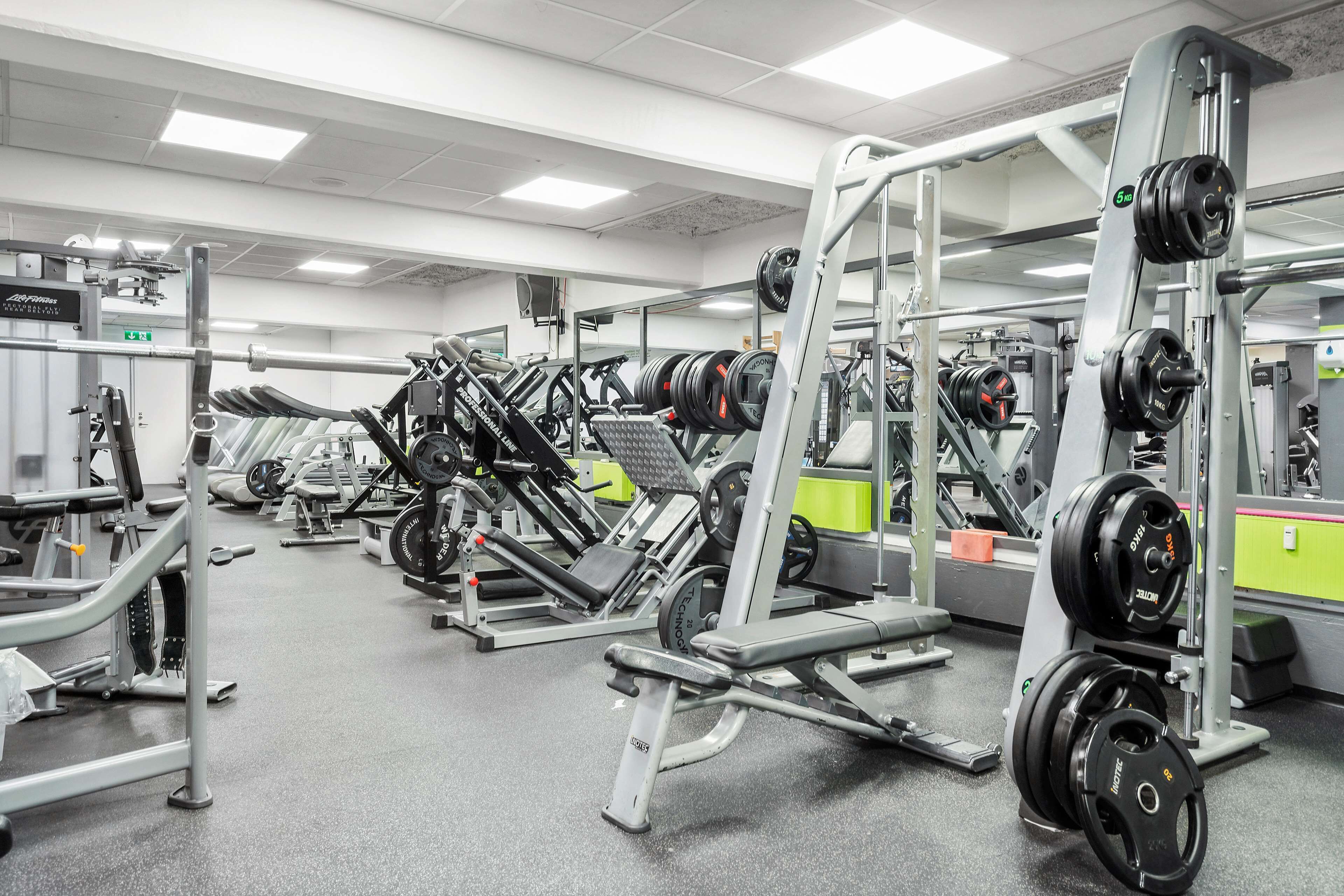 A gym with various exercise machines, weightlifting equipment, and mirrors.