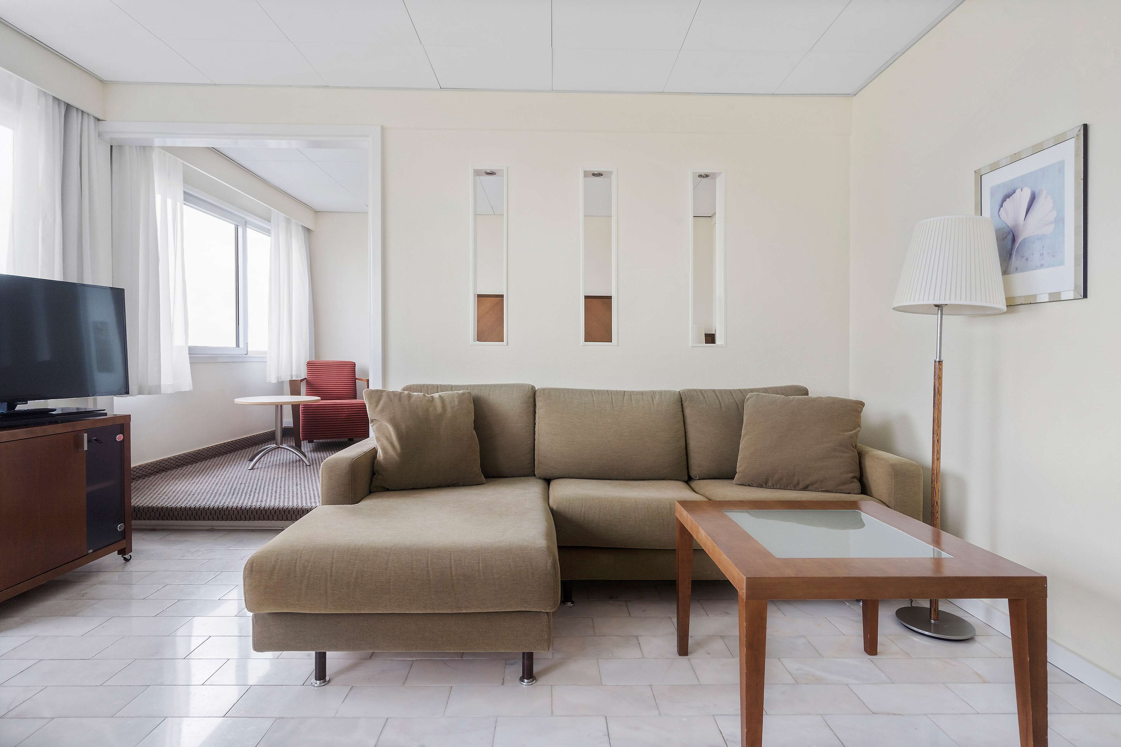 A modern living room with a sectional sofa, a wooden coffee table, a TV on a cabinet, and a red chair.