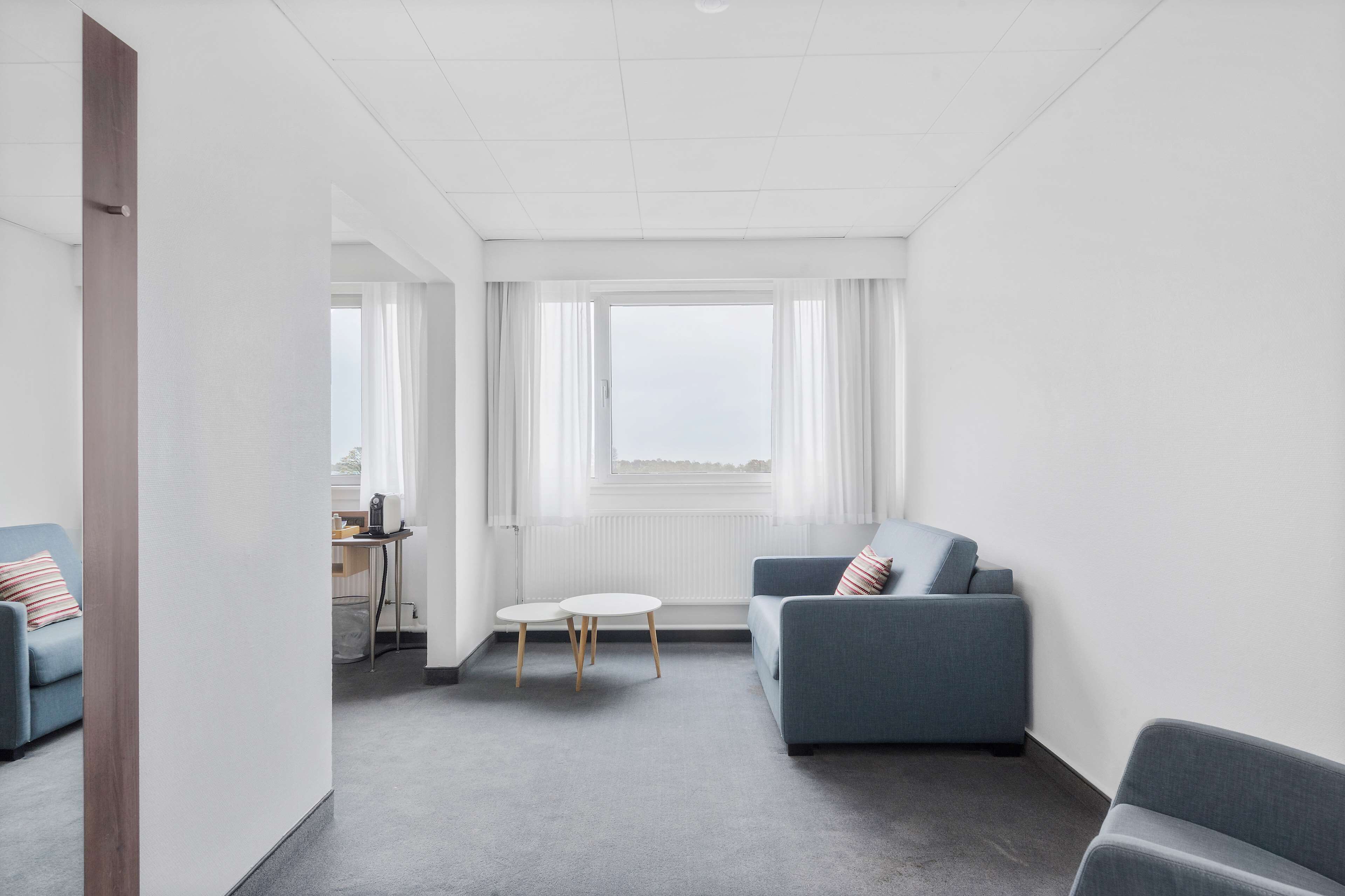 A modern, minimalist room with a grey sofa, a small round table, and a view through a large window.