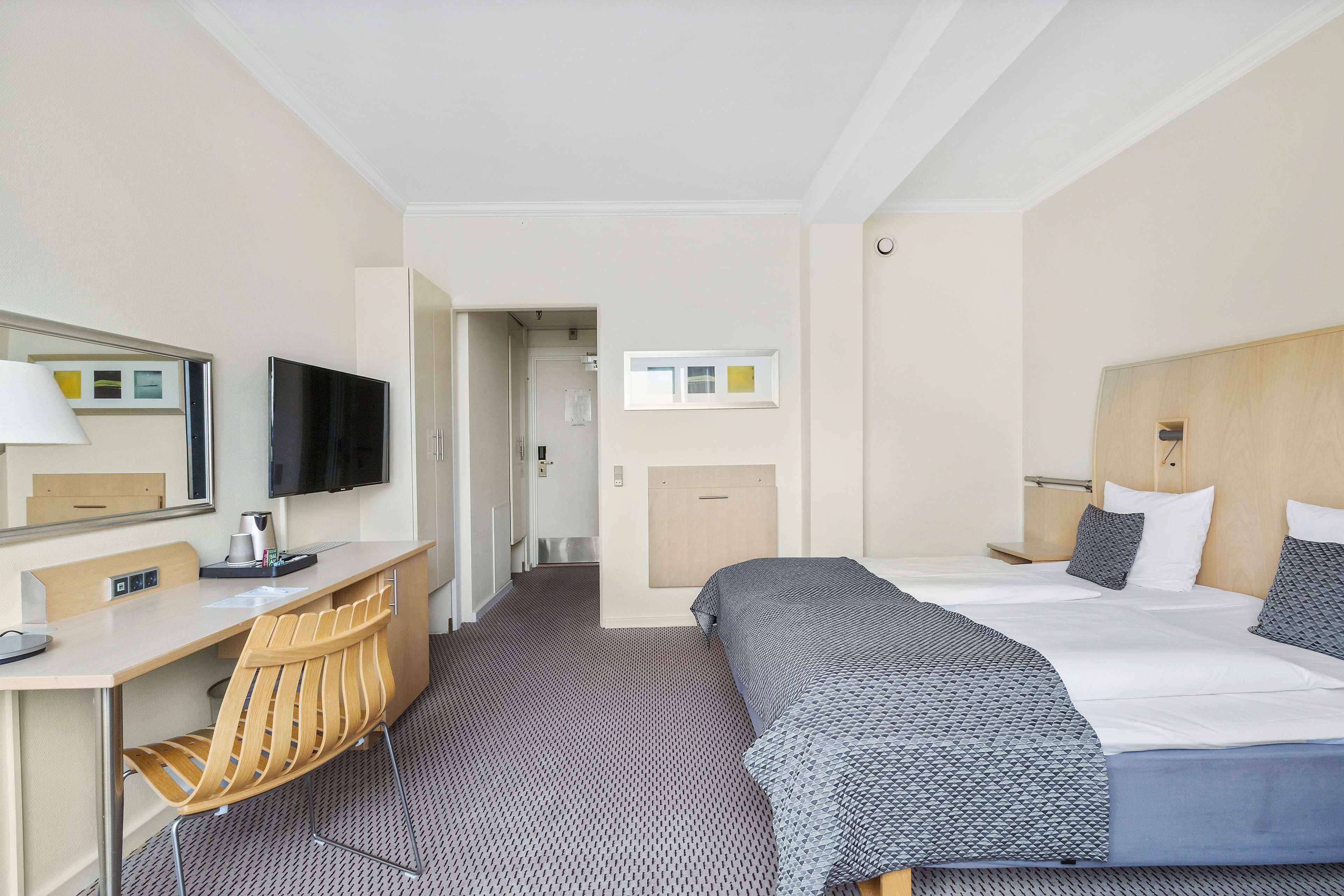 Une chambre d’hôtel avec un lit, un bureau, une chaise, une télévision et une petite fenêtre.