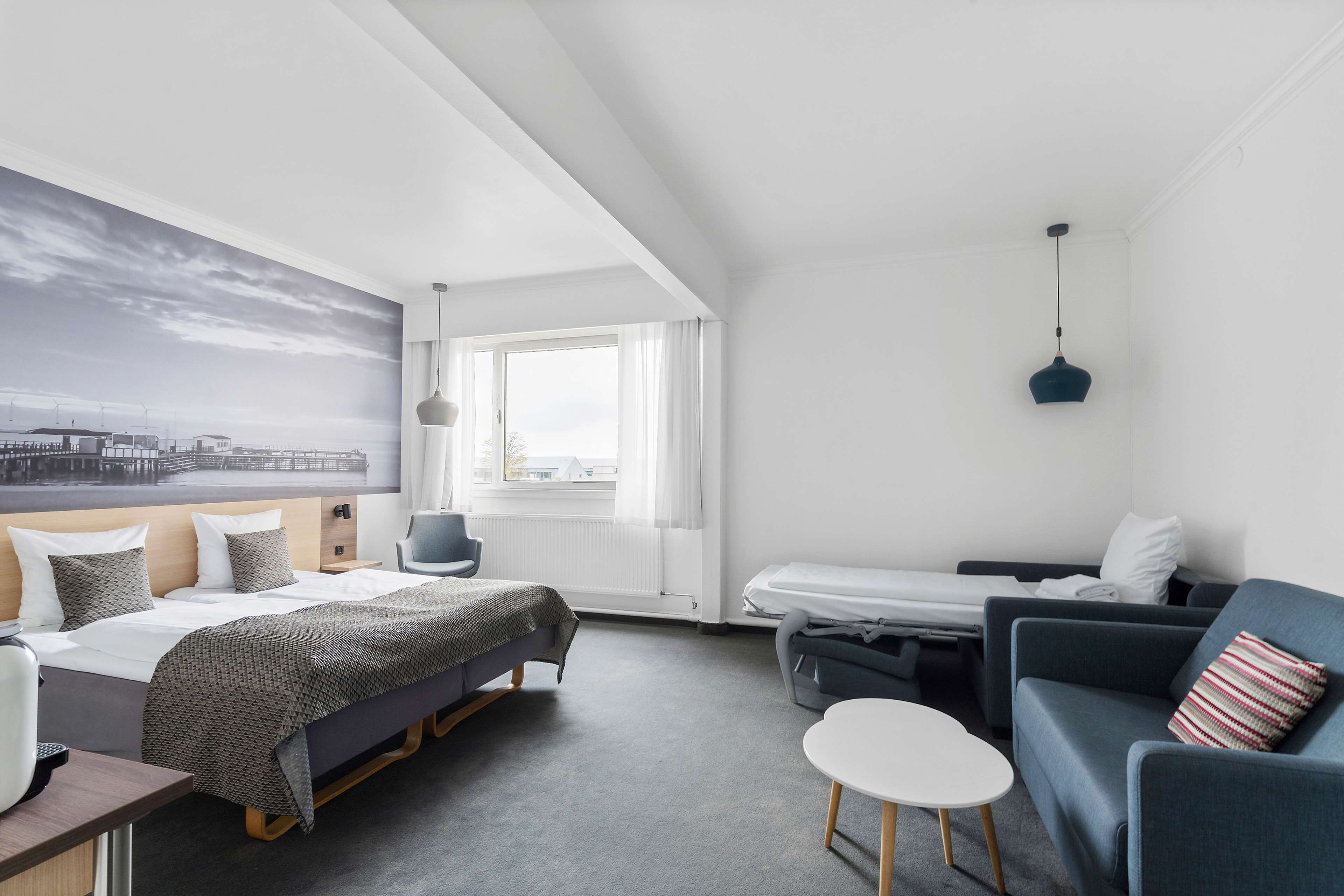 Habitación de hotel moderna con cama, sofá, una mesita y vistas a la ciudad a través de la ventana.