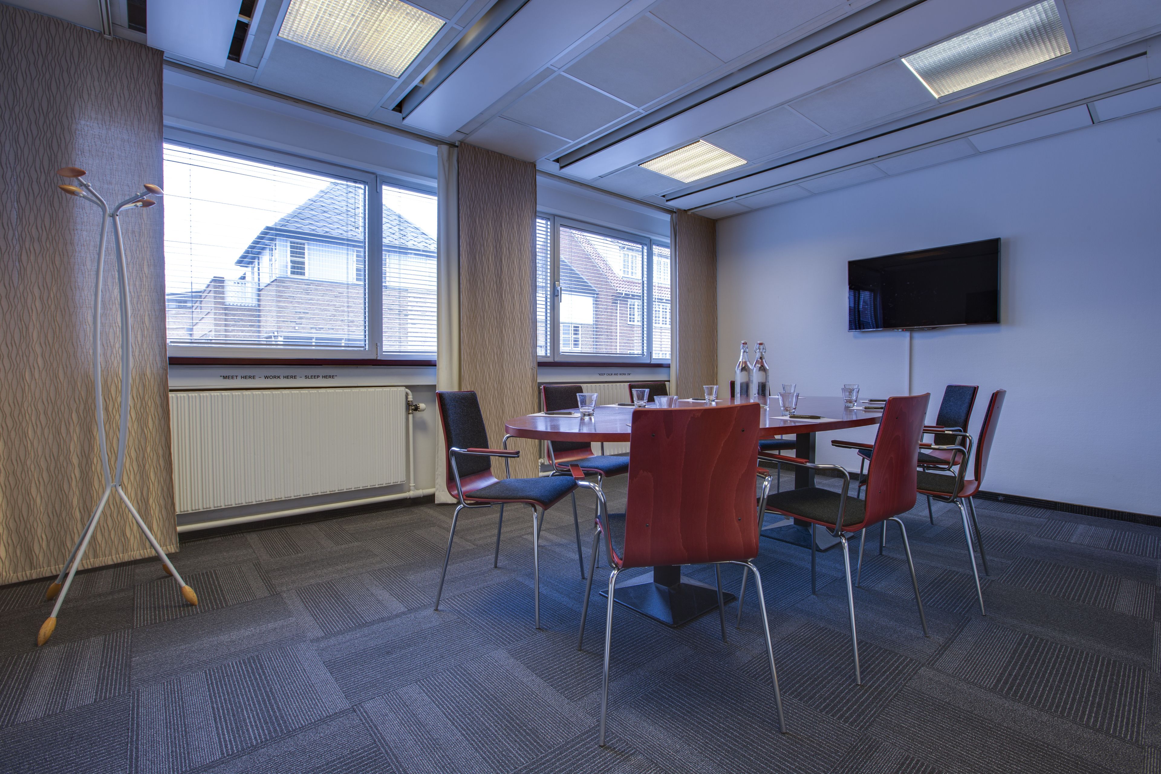 A conference room with a table, chairs, a standing lamp, and a television on the wall.