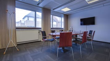 A conference room with a table, chairs, a standing lamp, and a television on the wall.