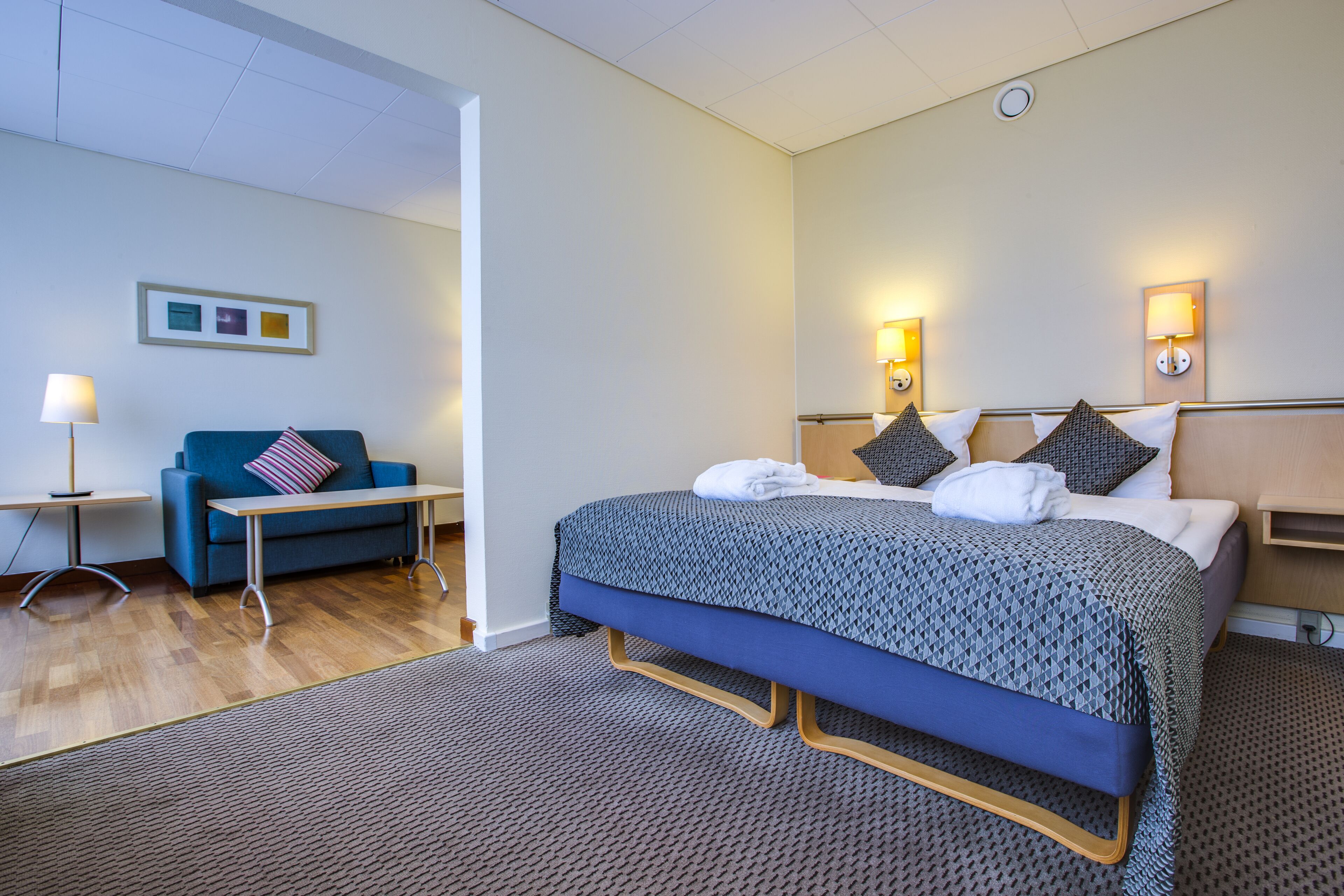 Een hotelkamer met een bed, een bank, een kleine tafel en een lamp.