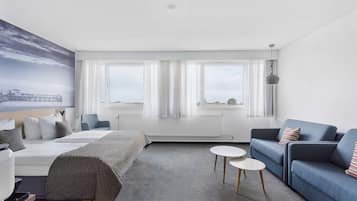 A modern hotel room with a bed, a blue sofa, a small white table, and large windows with curtains.