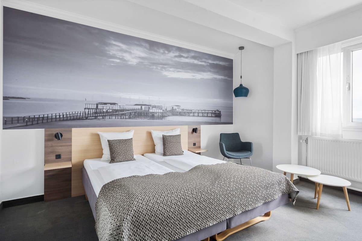 Une chambre d’hôtel moderne avec un grand lit, une petite table, une chaise et une grande œuvre d’art murale représentant une jetée.