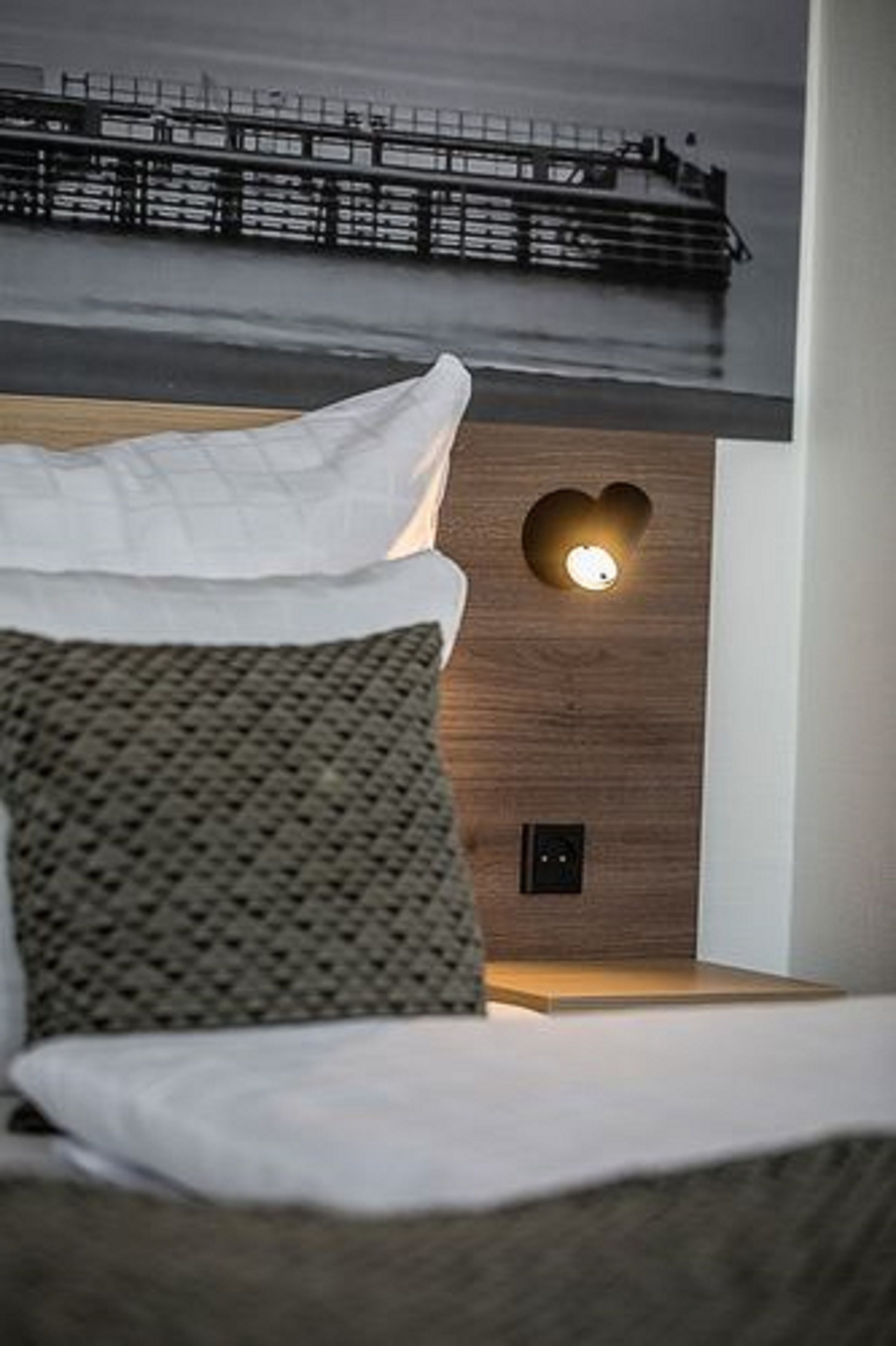 A bedroom with a bed, a heart-shaped wall light, and a view of a pier.