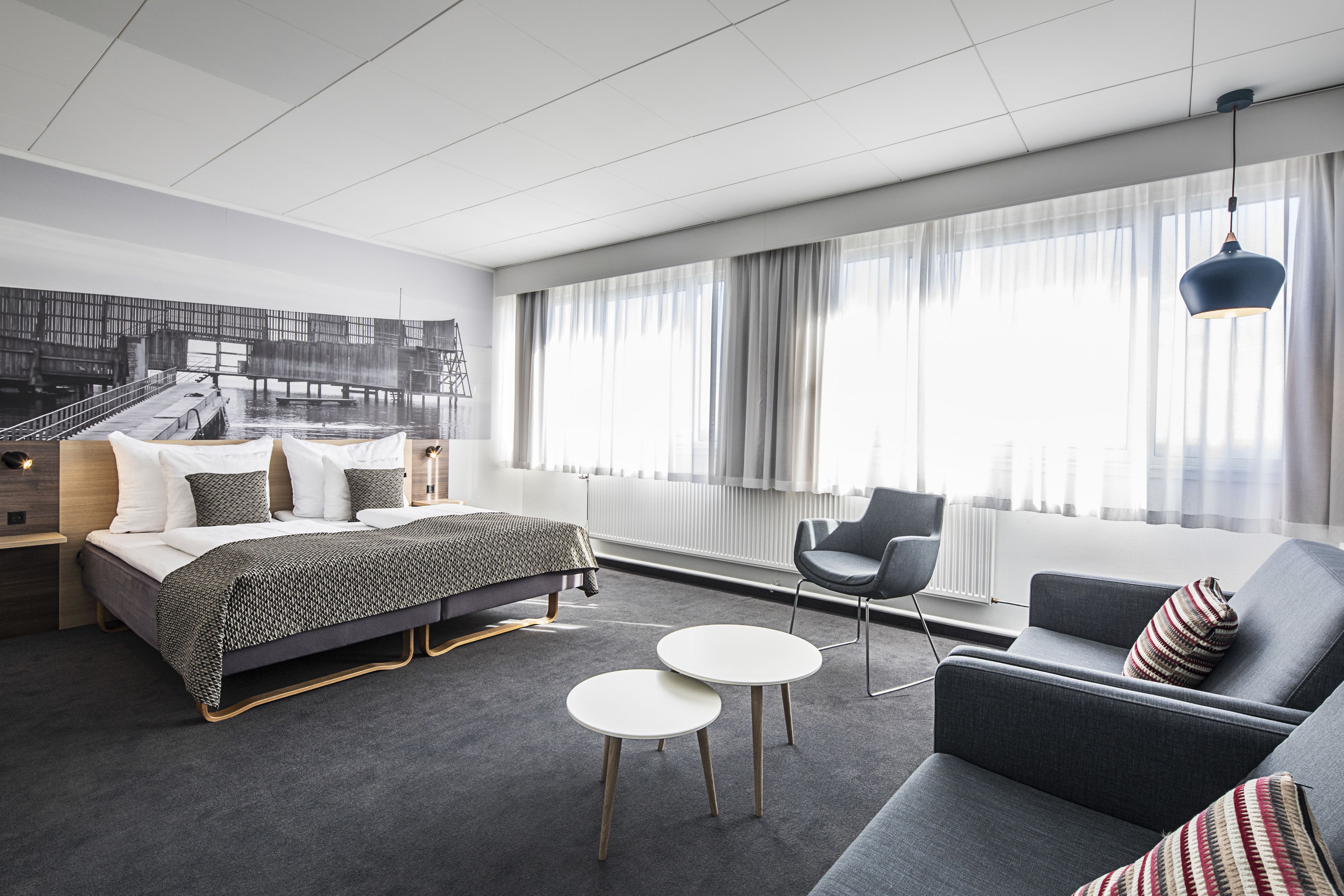 Ein modernes Hotelzimmer mit einem Bett, zwei runden Tischen, einer Couch und einem Sessel.